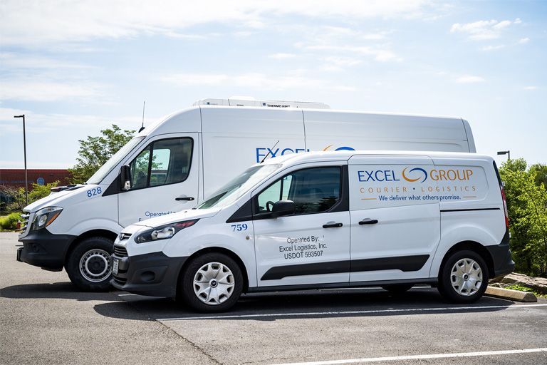 Två vita skåpbilar från Excel Group för bud- och logistiktjänster står parkerade.